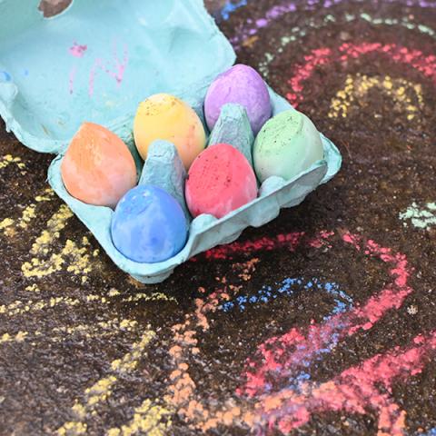 Chalk eggs in a box next to chalk drawings on the ground