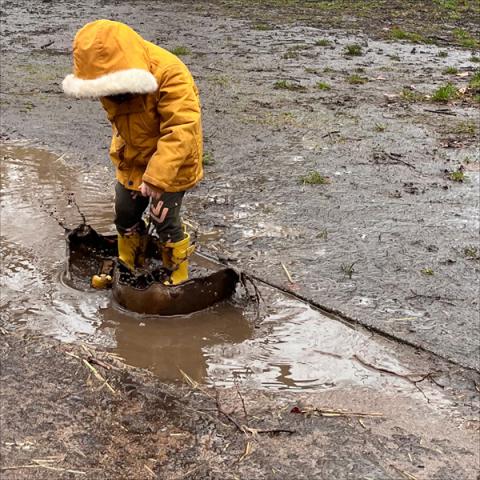 A child in a yellow coat jumps in a muddy puddle