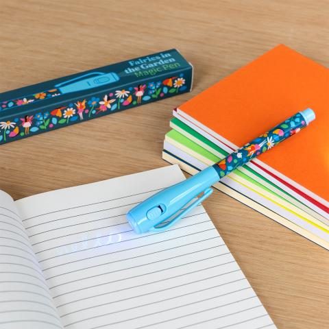 A fairy-design pen rests on a lined notebook, shining UV light on some writing