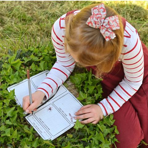 A young girl writes in a nature journal on the grass