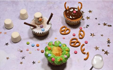 Three Christmas cupcakes sit on a table with marshmallow, stars and sprinkles