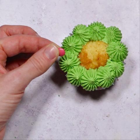A hand decorates a cupcake like a Christmas wreath