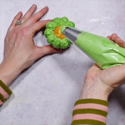 Hands pipe green icing onto a cupcake