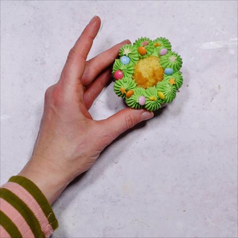 A hand hold a cupcake decorated like a Christmas wreath