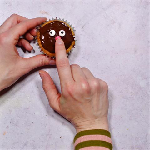 A hand places edible eyes onto a cupcake