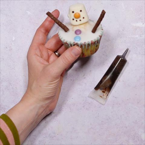 A hand holds a snowman cupcake