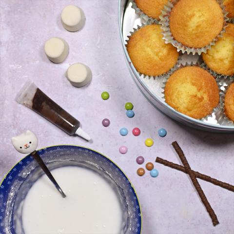 A table with cupcakes, marshmallows, icing and chocolate