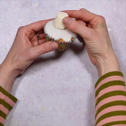 A pair of hands holds a cupcake with a marshmallow on it