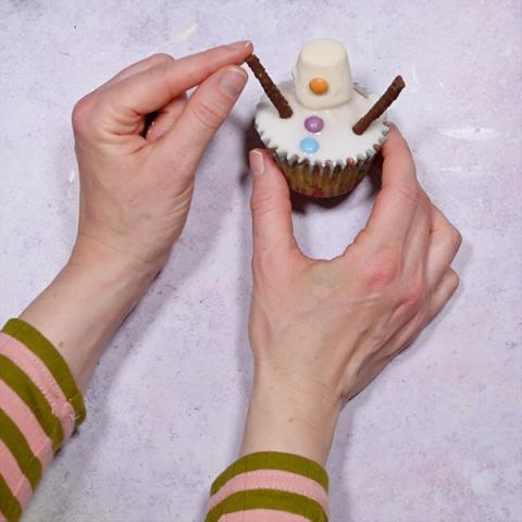 A pair of hands pushes some Matchmakers into a snowman cupcake