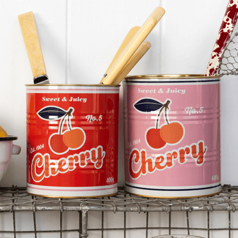 Two storage tins with a bold cherry print, filled with kitchen utensils