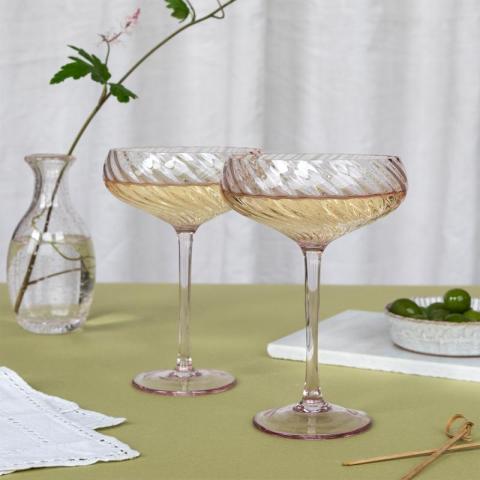 2 filled cocktail glasses next to vase on wooden table