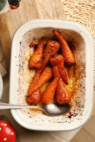 Carrots baked in a sauce in a white tray with spoon