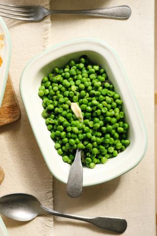 Green peas in a white serving dish with spoon