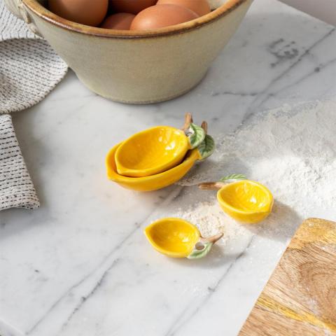 Lemon shaped yellow measuring spoons on kitchen surface next to eggs