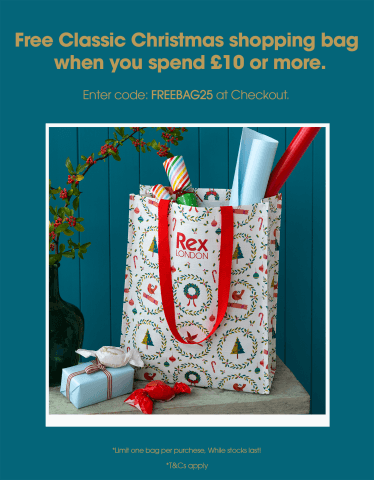 A festive gift bag with red handles and a holiday-themed pattern featuring wreaths, trees, and candy canes. The bag is labeled “Rex London” and filled with colorful wrapping paper and small gifts, placed on a wooden surface beside wrapped presents and candies.
