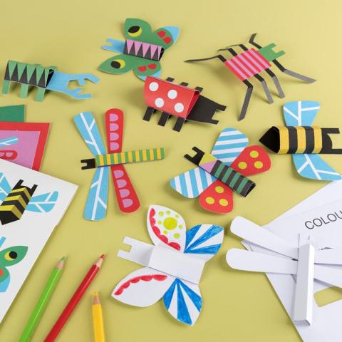 Cardboard bugs floating around with pieces of paper and pencils