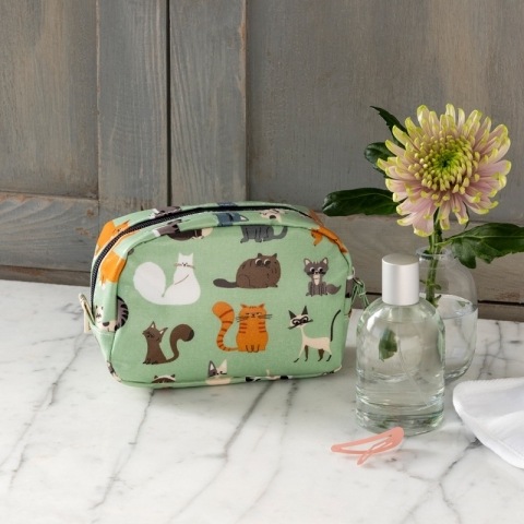 Green make up bag with cats next to flower and perfume