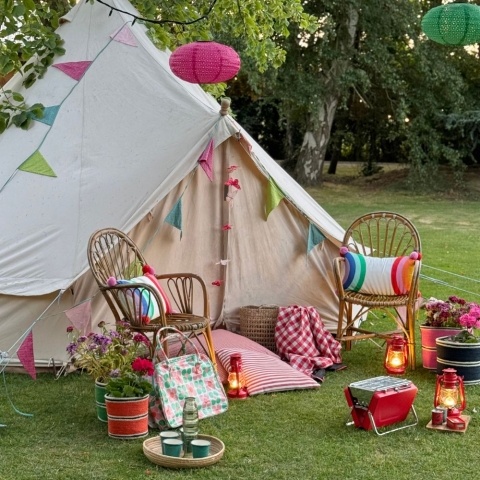 A large tent with chairs, a portable barbecue, cushions and lamps in front