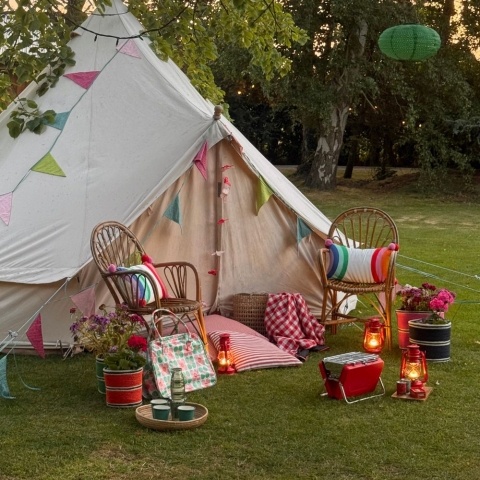A large tent with chairs, a portable barbecue, cushions and lamps in front