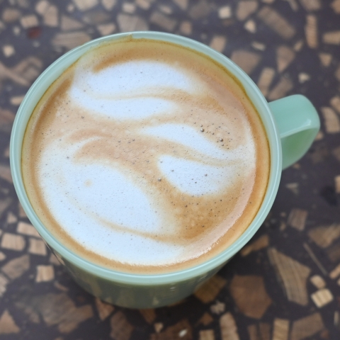 A top down shot of a green mug with leaf latte art