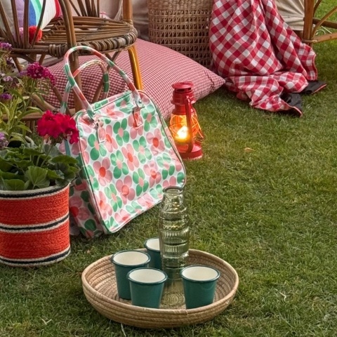 A woven tray holds four green tumblers. It sits on a lawn with a colourful bag and basket in the background
