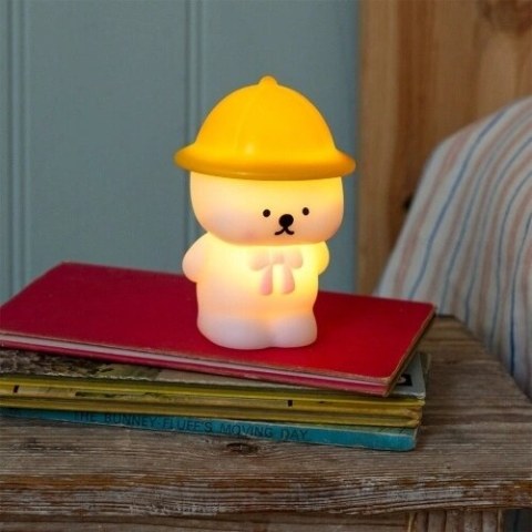 Little Bear night light glowing on a stack of books beside a bed.