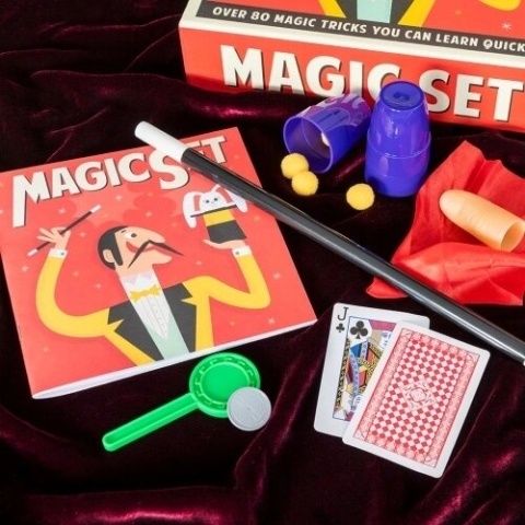 Magic set contents including a wand, cups, sponge balls, a scarf and playing cards, laid out on red velvet.