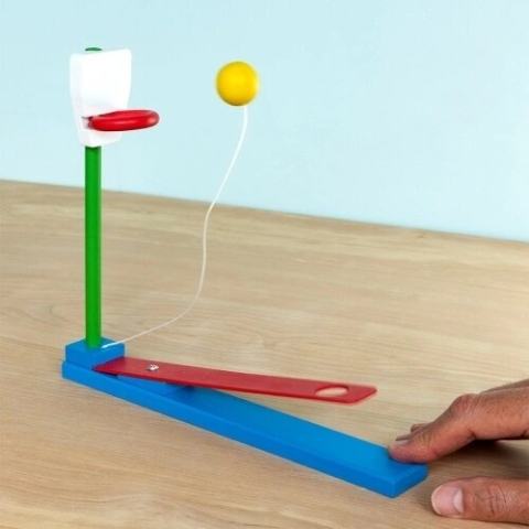 Wooden tabletop basketball game, with a hand pressing the lever to launch the ball towards the hoop.
