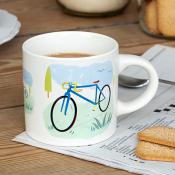 White ceramic mug with a colorful blue bicycle illustration, filled with a hot beverage.