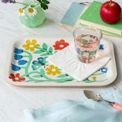 Wooden serving tray holding a glass of water and a folded white napkin on a colourful floral-patterned surface.
