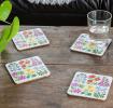 Four white wood and cork coasters featuring floral pattern on table with drink