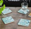 Four blue-green wood and cork coasters featuring dog pattern on table with drink