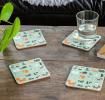 Four light green wood and cork coasters featuring cat pattern on table with drink