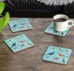 Four light blue wood and cork coasters featuring garden bird pattern on table with drink
