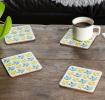 Four cream wood and cork coasters featuring bird pattern on table with drink