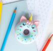 Doughnut-shaped unicorn eraser placed on a notebook beside coloured pencils.