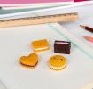 Four biscuit-shaped erasers in different styles and colours, placed on a notebook 