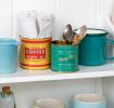Two vintage coffee tins repurposed as utensil holders on a kitchen shelf.