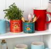 Mini honey storage tins repurposed as herb and utensil holders on a kitchen shelf.