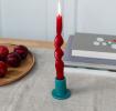 ceramic candle holder with a cylindrical shape and wide flat base, holding a lit red candle