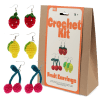 Crochet kit packaging placed beside three finished crocheted earrings shaped like strawberries, lemons, and cherries
