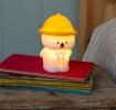 White bear night light wearing a yellow hat and pink neck tie shown with light on