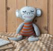 Knitted monkey toy with a grey body and wearing an orange and grey striped shirt.