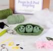 Crochet kit packaging placed beside finished green peas in a pod keychain 