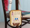 Beige and yellow crossbody bag with a front pocket featuring a smiling face design and two small brown plush feet at the bottom.