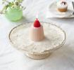 Pink jelly-shaped candle topped with a decorative red strawberry displayed on a decorative cake stand.