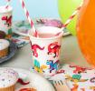 Dinosaur‑themed party paper cup with matching paper plate and napkins beside it.