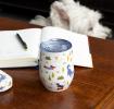 Travel cup with playful dog illustrations on a wooden table.