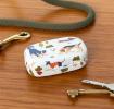 Mini travel case with playful dog illustrations on a wooden surface beside keys.