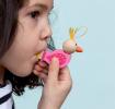 Child blowing a bird‑shaped wooden whistle with a pink body, wooden head, and orange beak.